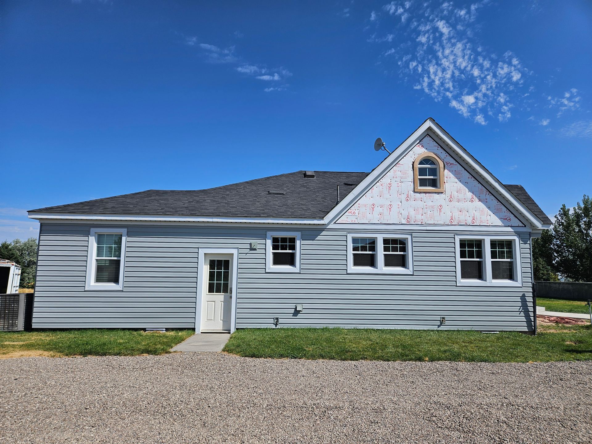 A house with a lot of windows is sitting on top of a gravel lot.