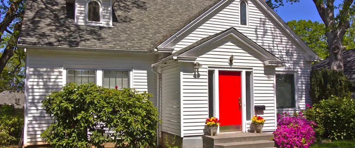 A white house with a red door and flowers in front of it.