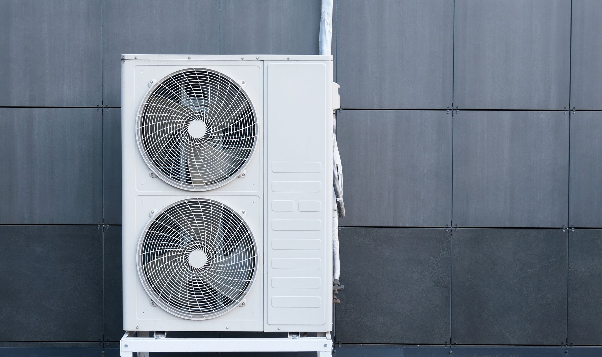 Deux grands ventilateurs de condenseur de climatisation extérieurs montés sur un boîtier blanc contre un mur carrelé foncé