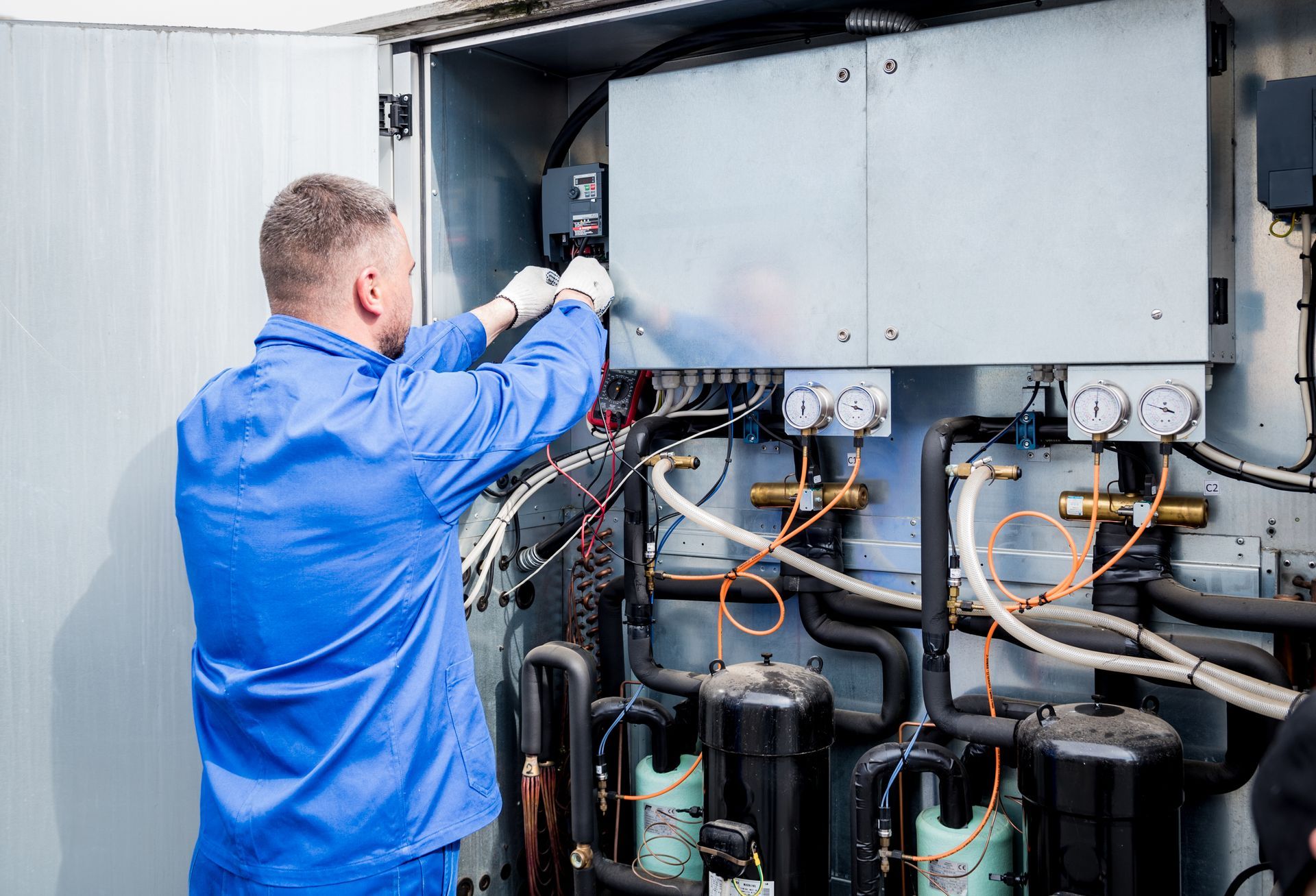 Un technicien inspecte une unité de climatisation industrielle à l'aide d'outils et de câbles apparents.