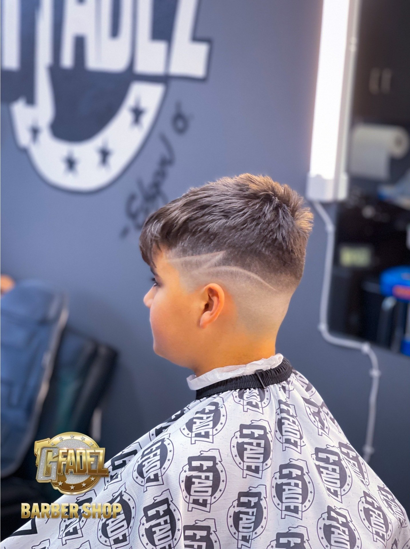 Side view of a child getting a haircut, wearing a patterned barber cape in a barbershop.