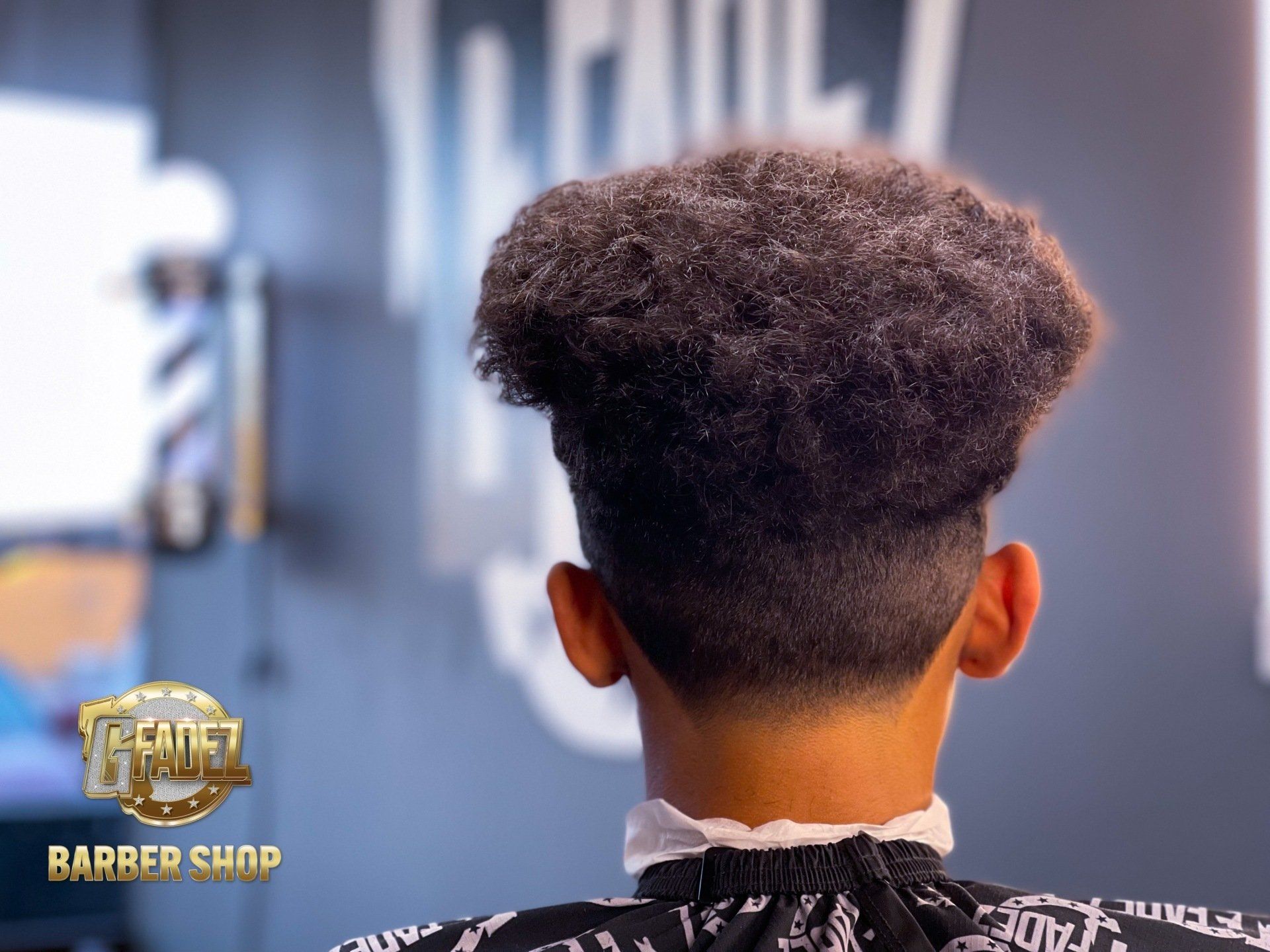 Back of a person with a high curly fade haircut in a barbershop chair