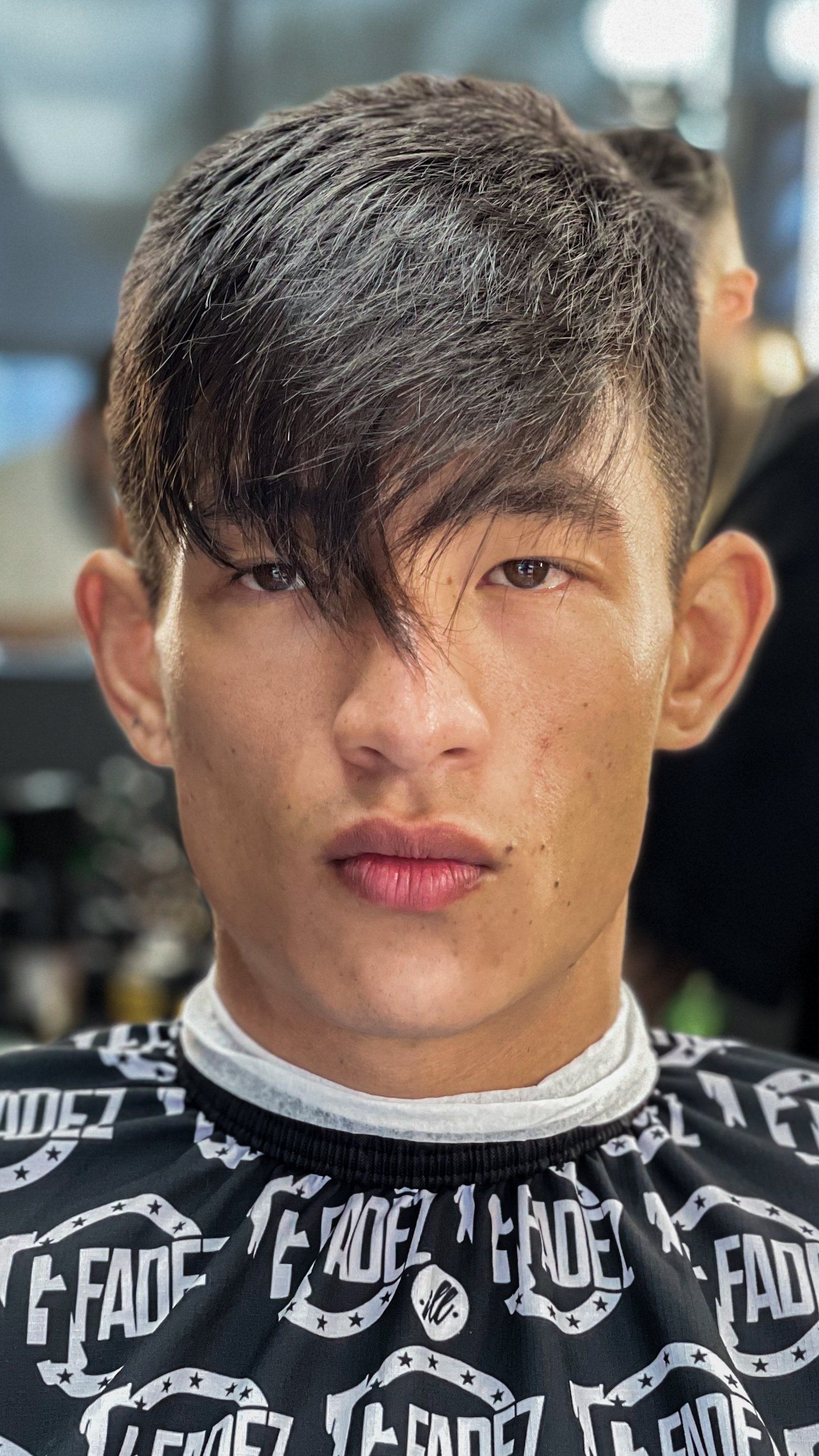 Close-up of a person with wet hair and a neutral expression, wearing a black patterned shirt indoors.