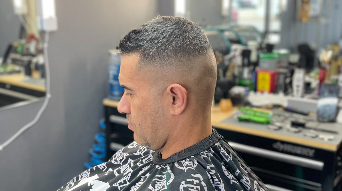 Man in a barber chair wearing a patterned cape, shown in profile with a short fade haircut in a salon.