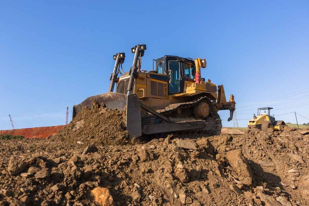 A Bulldozer Is Moving Dirt In A Muddy Field — A2Z Property Services In Gympie, QLD