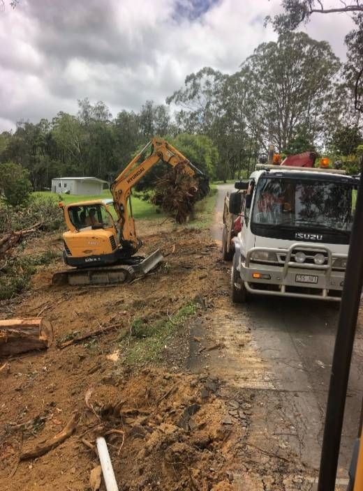 A Truck Is Driving Down A Dirt Road Next To A Yellow Excavator — A2Z Property Services In Woolooga, QLD