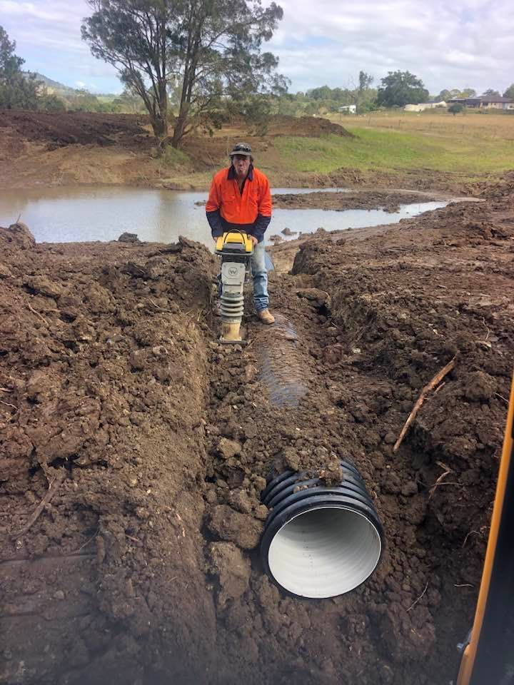 A Worker Compacting Soil Over a Pipe in A Trench with A Compactor — A2Z Property Services In Cooroy, QLD