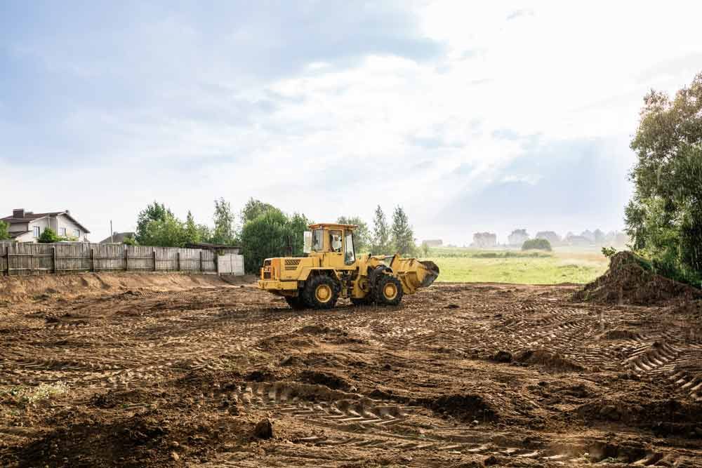 A Yellow Bulldozer Is Driving Through A Dirt Field — A2Z Property Services In Kybong, QLD