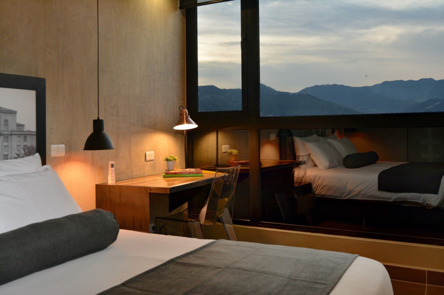 Habitación de hotel moderna con dos camas, lámpara de escritorio y vistas a la montaña a través de grandes ventanales.