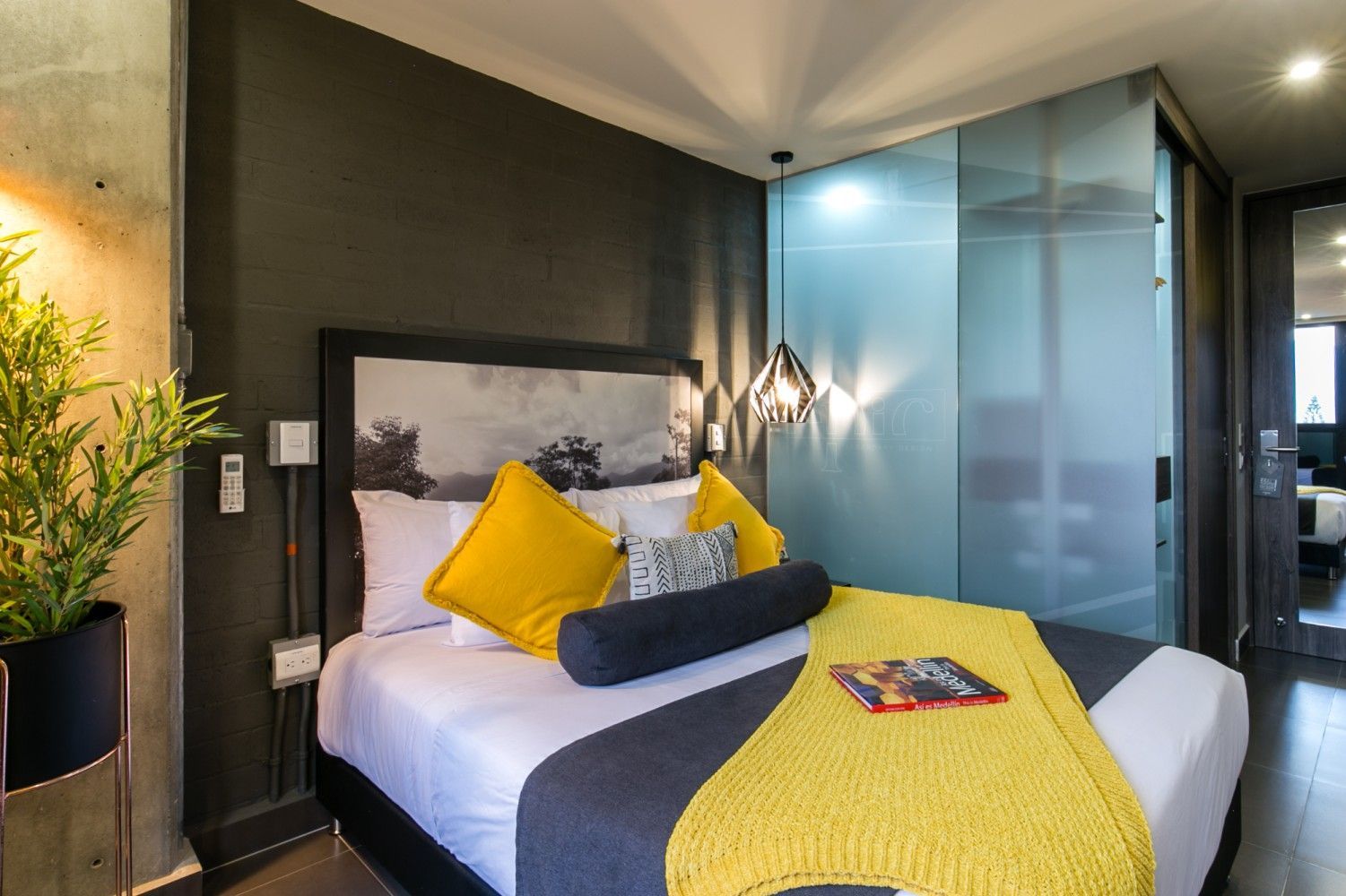 Dormitorio moderno con cama, detalles en amarillo, paredes oscuras y puertas de vidrio esmerilado.