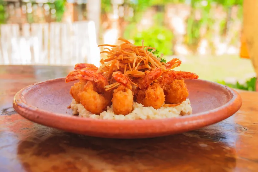 Um prato de comida com camarão e arroz em uma mesa de madeira.-Pousada-Bangalos-do-Pontal