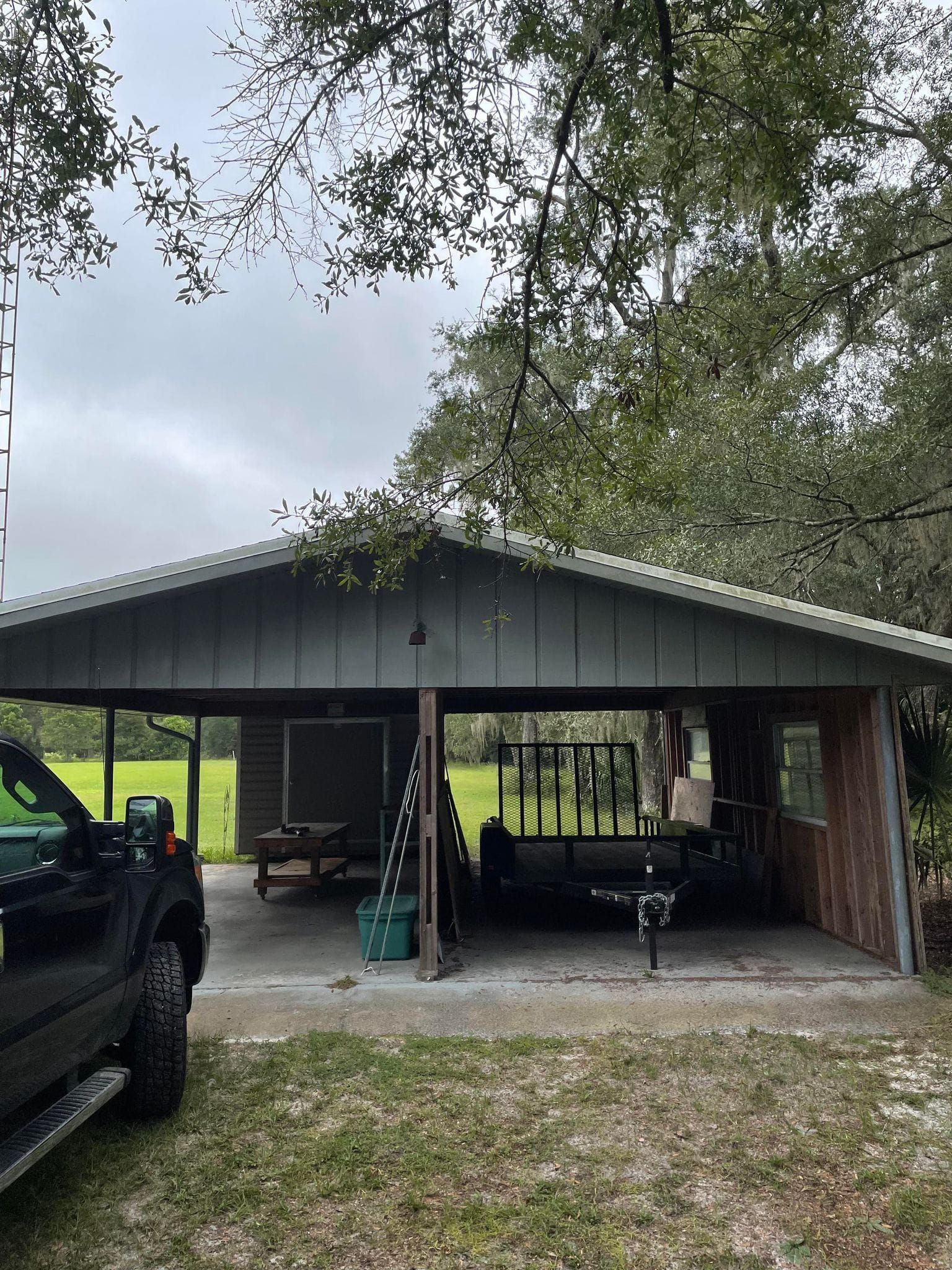 Carport with a metal roof, parked truck, and trailer under a cloudy sky.