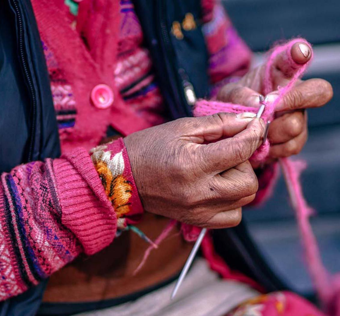 Hands knitting with pink yarn, holding a needle, wearing a pink sweater.