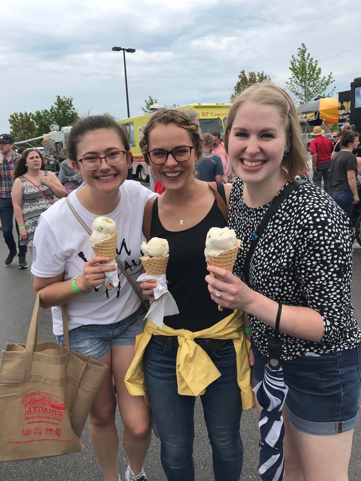 Three people smiling, holding ice cream cones, at an outdoor food event.