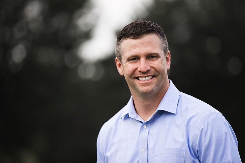Man in light blue shirt smiles outdoors.