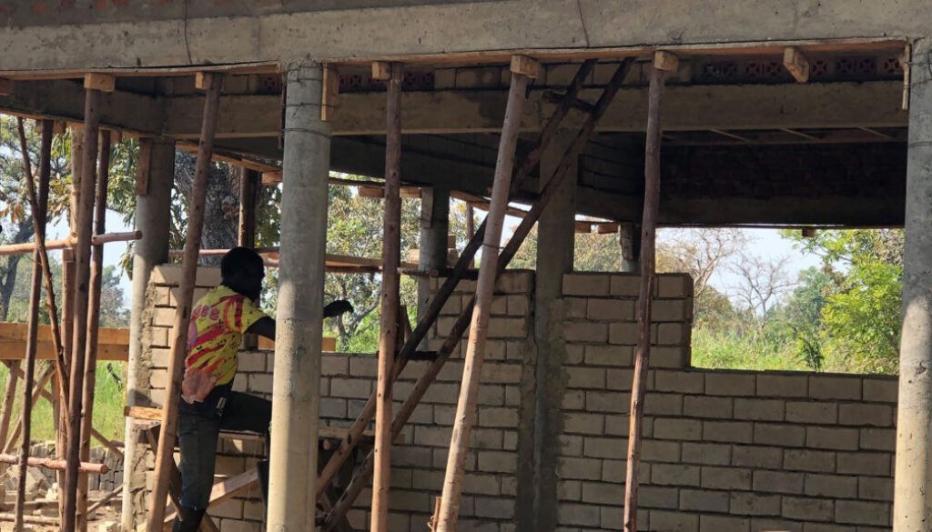 Blog 7 Construction worker near a building site. Wooden supports, brick wall. Light environment.
