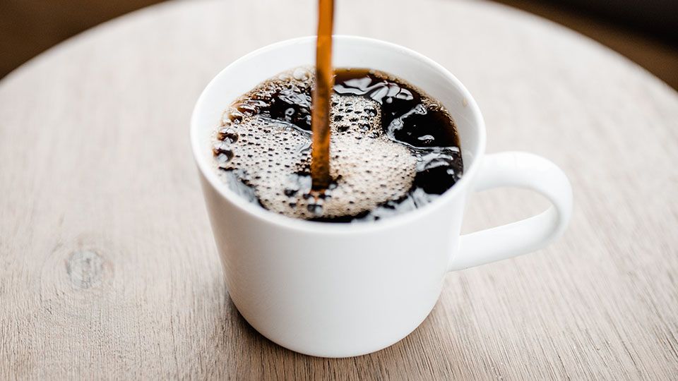 Coffee being poured into a white mug on a wooden surface.