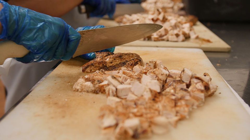Person in blue glove cuts diced meat on a cutting board.