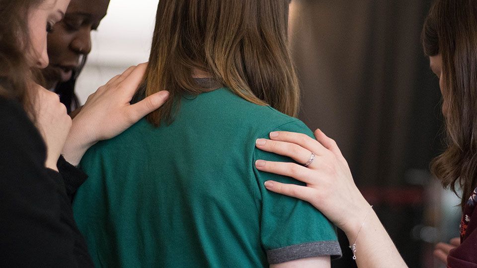 Group of people supporting someone, hands on shoulders, indoors.