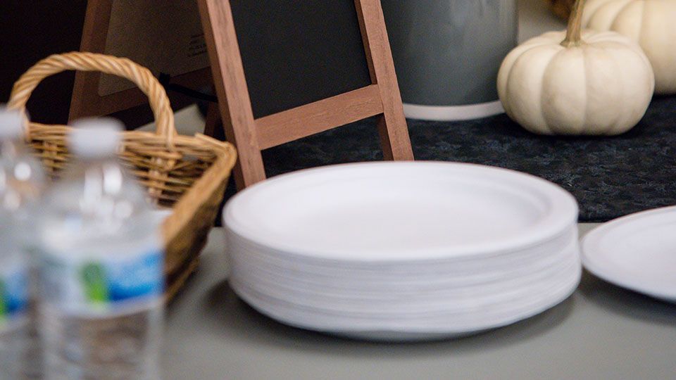 Stack of white paper plates on a table next to water bottles and fall decorations.