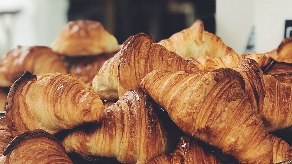 Golden-brown croissants piled up, showing flaky layers, likely in a bakery.