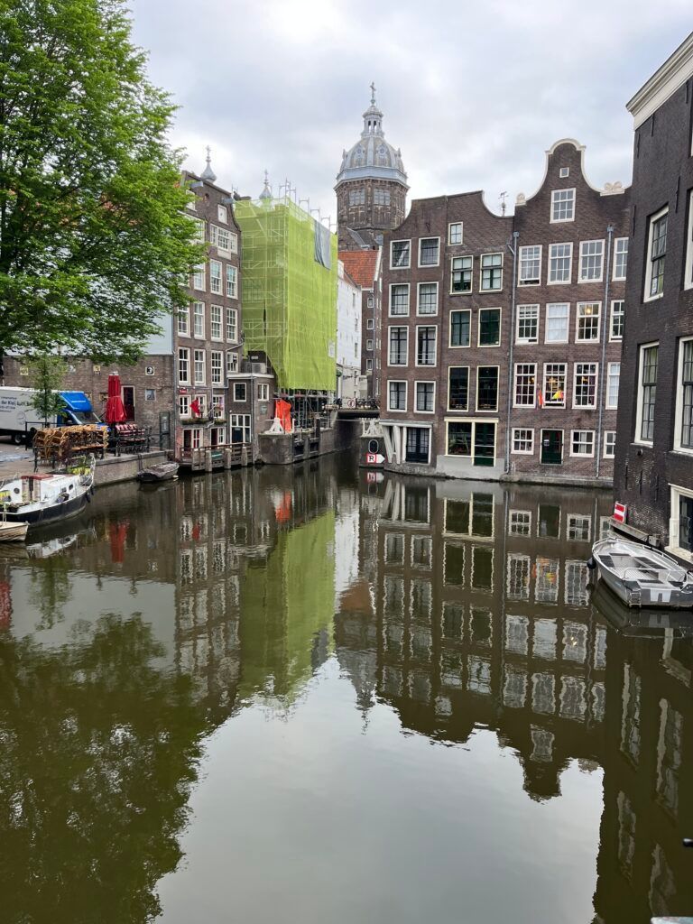 Canal in Amsterdam reflects historic buildings, cloudy sky.