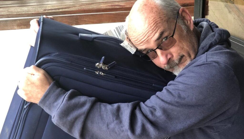 Post4 Man hugging a large blue suitcase, looking strained.