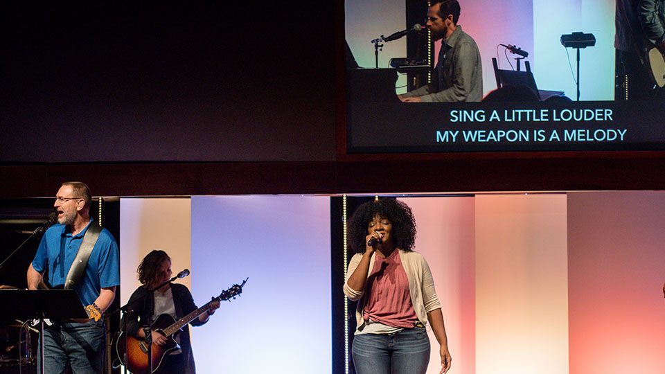 Worship band performing on stage with a screen displaying lyrics.