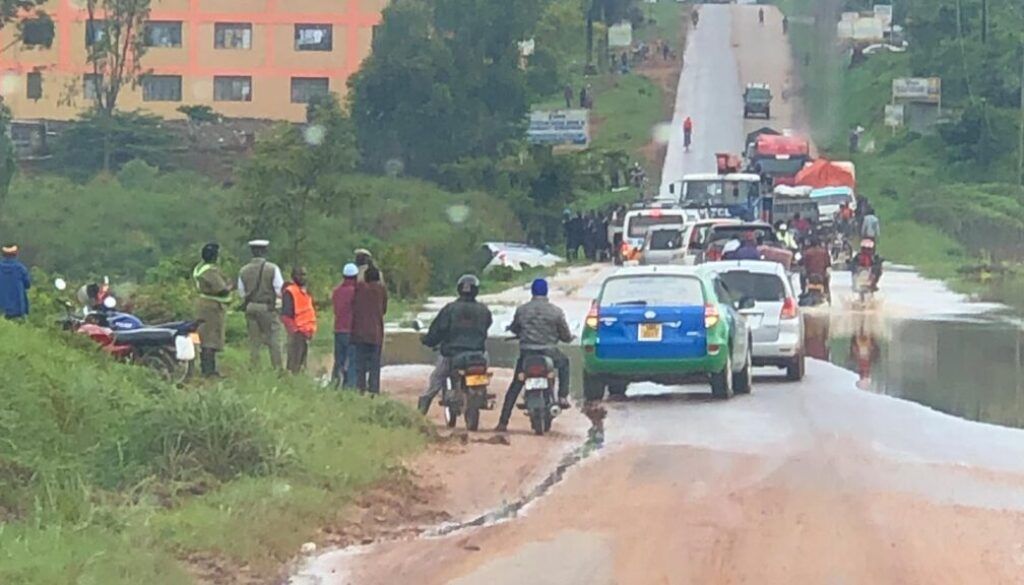 Trip2 copy Cars and motorcycles stuck in traffic on a flooded road, people on the roadside, and buildings in the background.