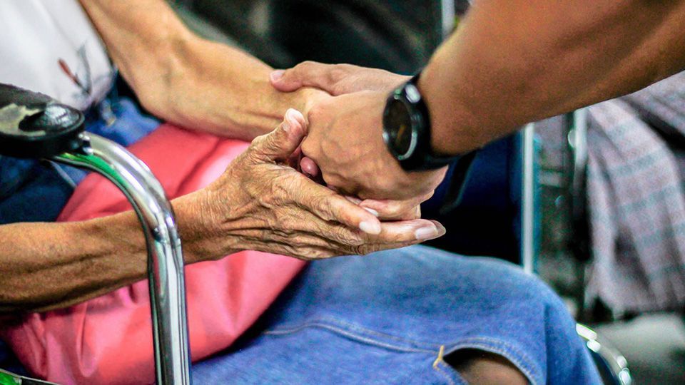 Person holding the hands of an elderly person in a wheelchair.