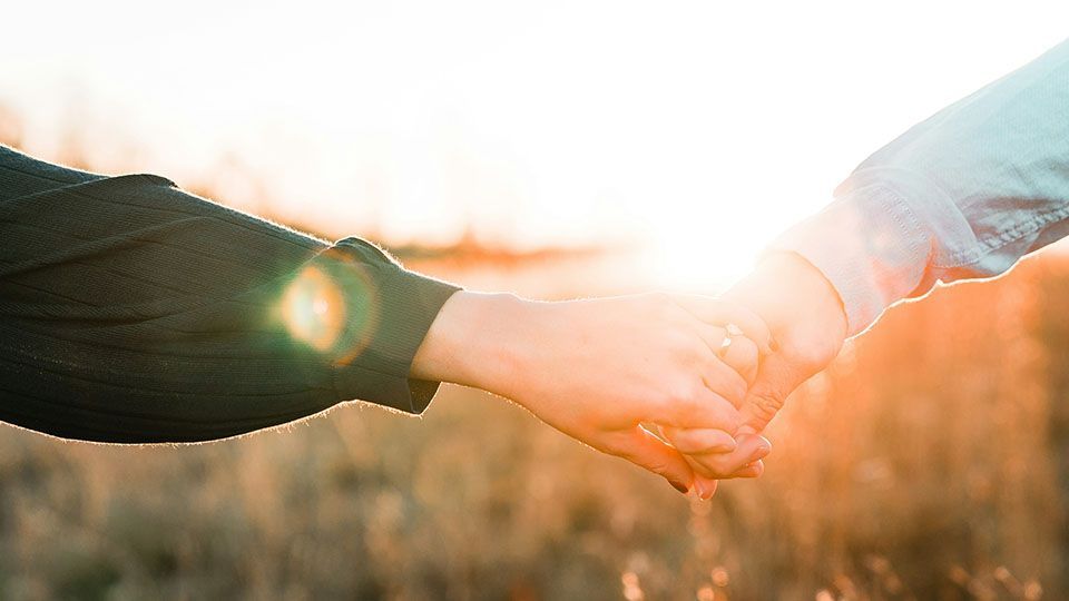 Two hands clasped, bathed in warm sunlight over a field.