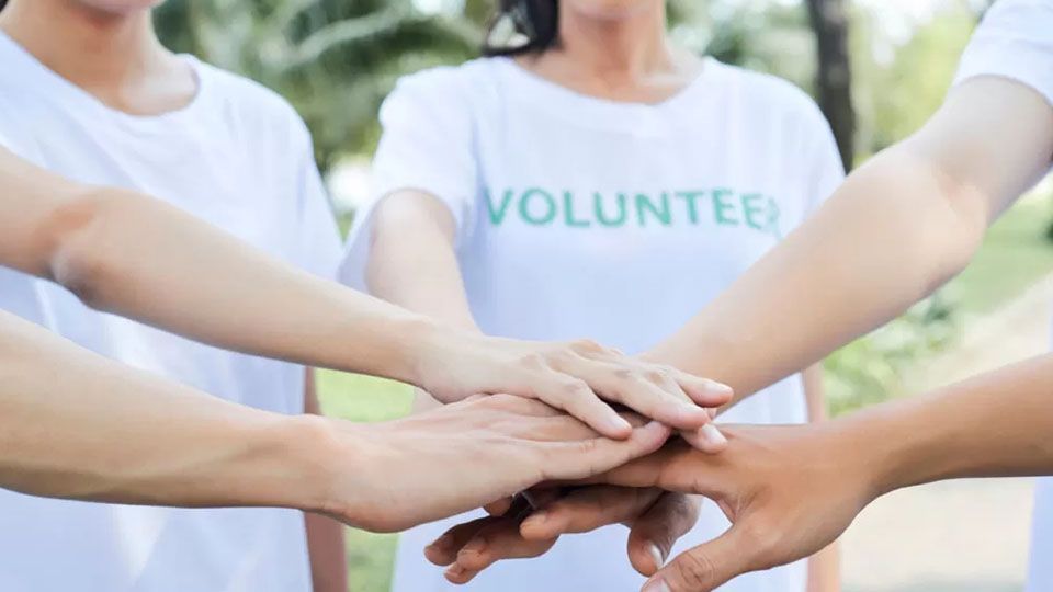 Volunteers with hands stacked together; one person wears a shirt that says