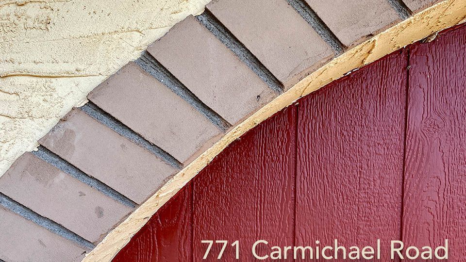 Close-up of a red wooden door, arched brickwork, and a section of cream-colored stucco wall.