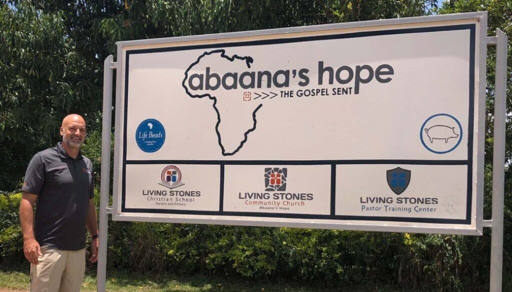 post e Man standing next to a sign for Abaana's Hope, with the outline of Africa.