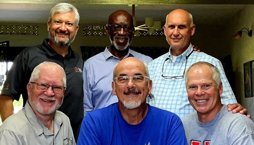 Group of six men smiling, posing together indoors.