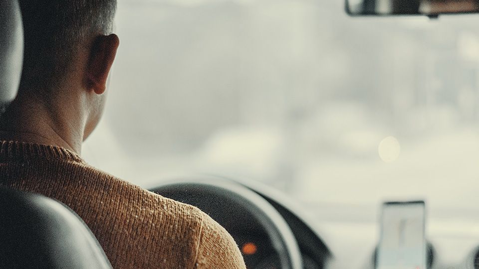 Man driving a car, blurred street scene visible through the window.