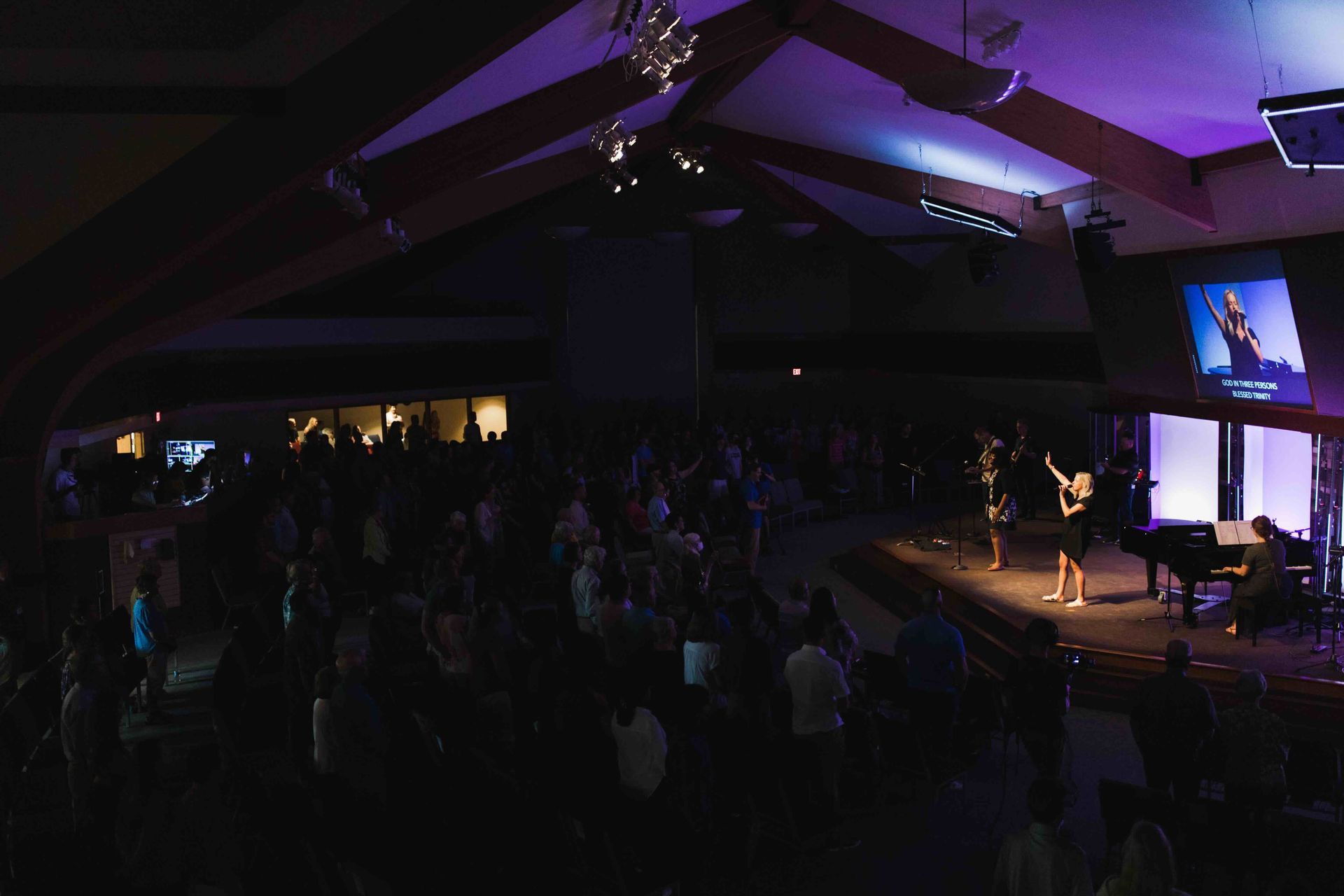 Audience at a concert; musicians on stage with purple lighting.