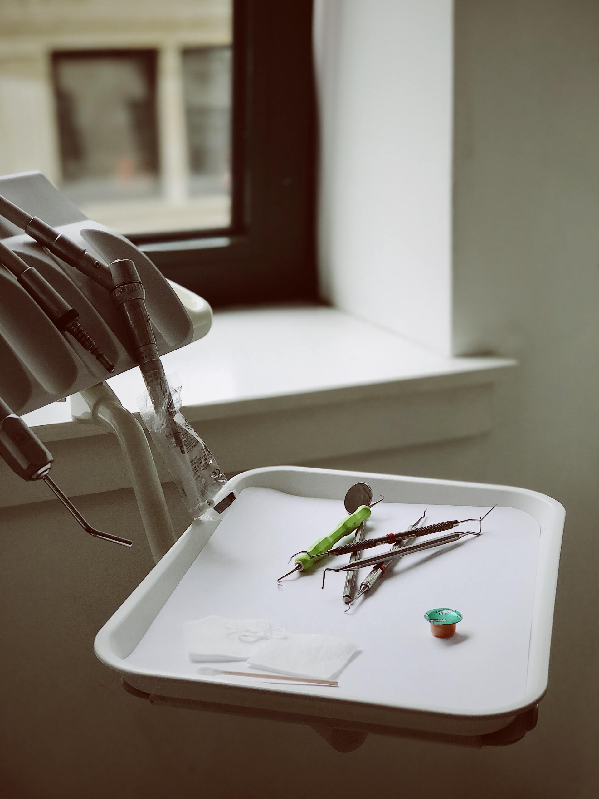 A gloved hand pouring liquid into a white tray with small tools near a window