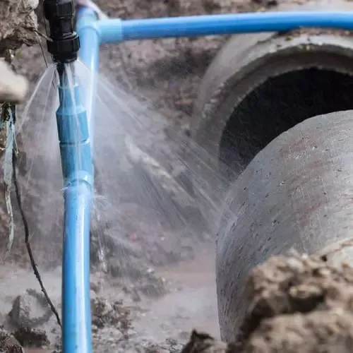A blue pipe is leaking water into a concrete pipe.