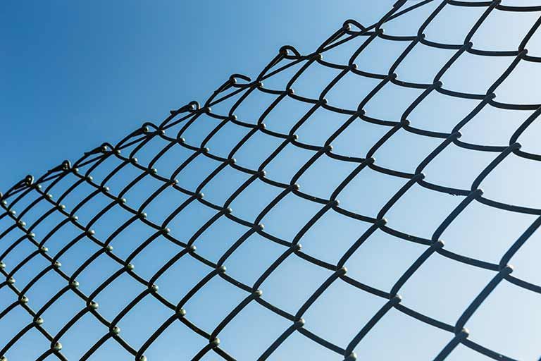 Close-up of a chain-link fence angled against a clear blue sky.