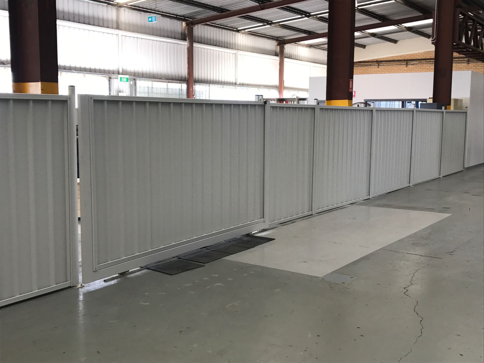 A row of grey, corrugated metal partition panels installed on a concrete warehouse floor.