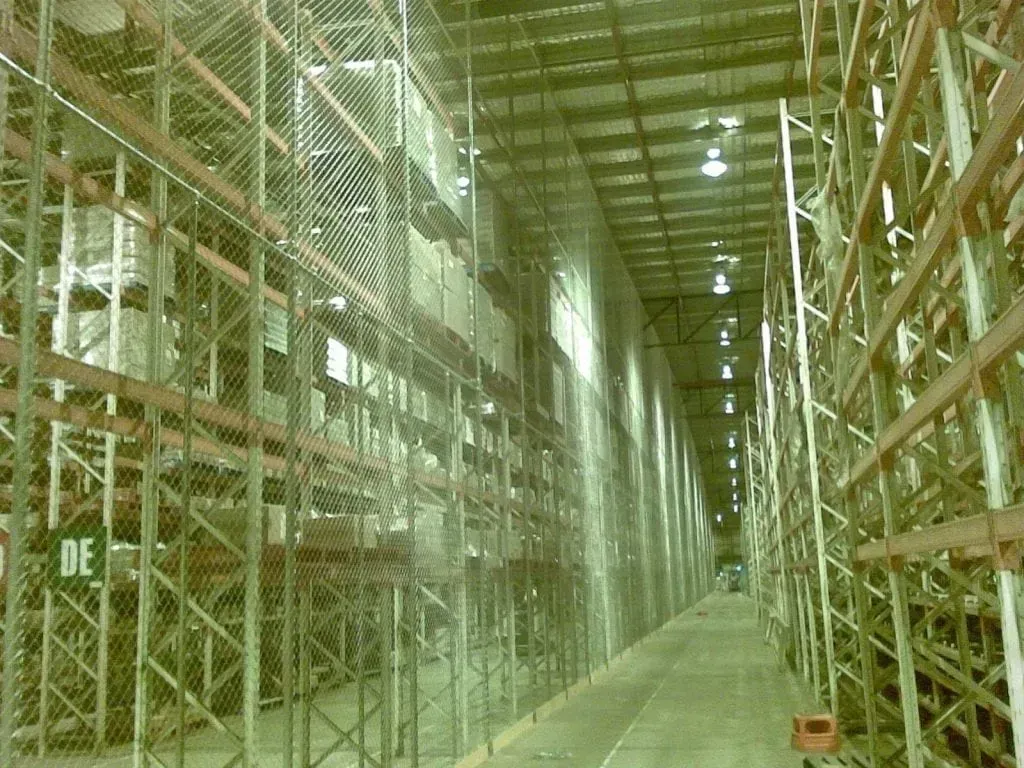 An aisle in a large warehouse featuring tall industrial metal shelving units on both sides and safety netting.