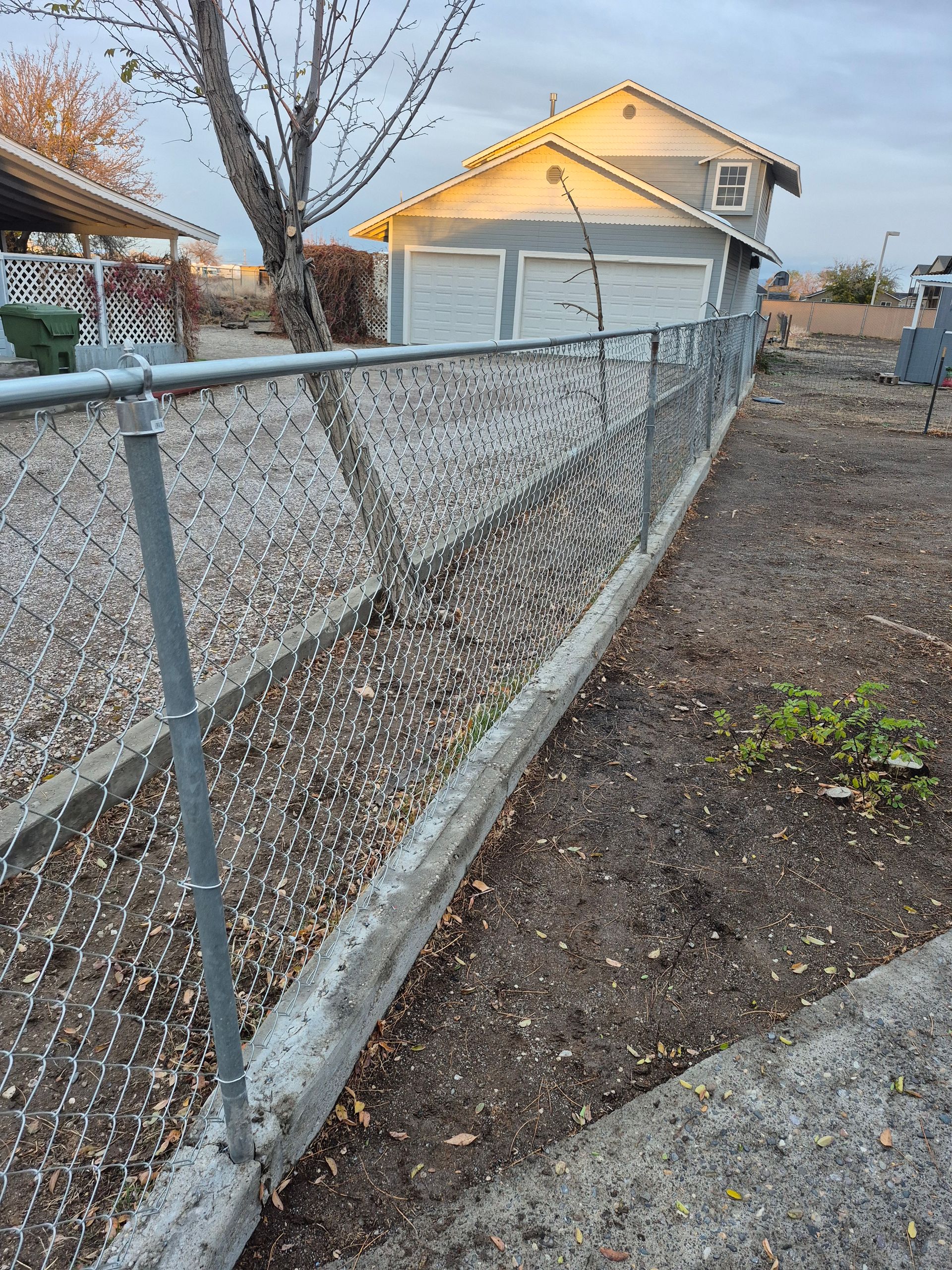 Chain-link fence borders a dirt area next to a garage with two doors; overcast sky.