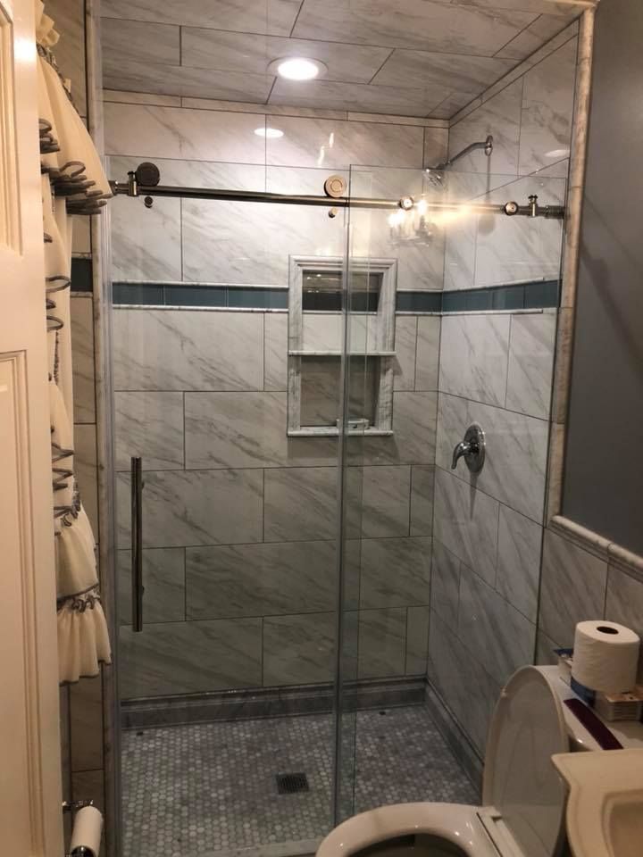 Bathroom with marble tile shower, glass door, toilet, and white door.