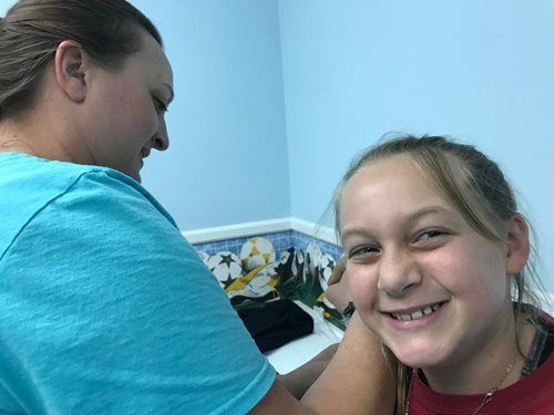 Smiling girl getting her ear pierced while another woman assists in a blue room