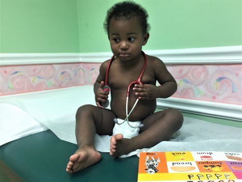 Child holding a stethoscope while sitting on a medical examination table in a clinic room