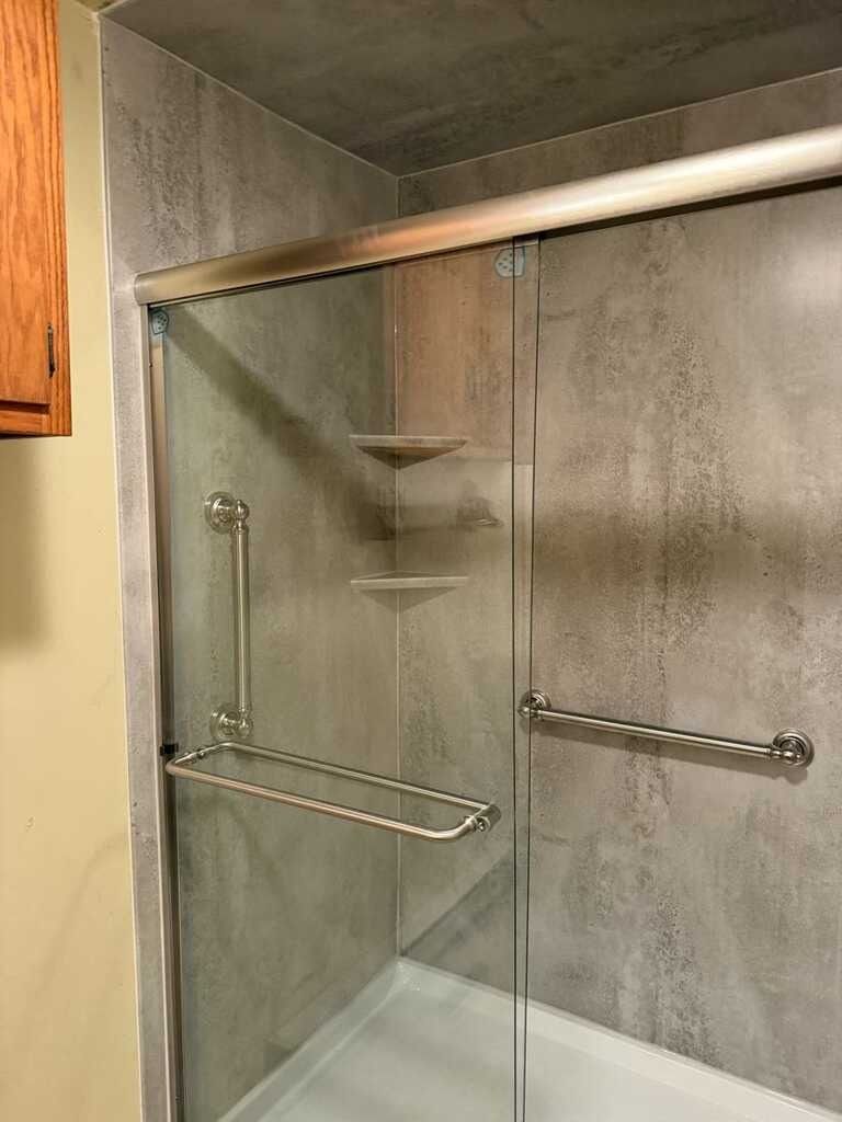 Accessible shower with glass doors, grab bars, and built-in shelves. Gray walls, and a silver frame.
