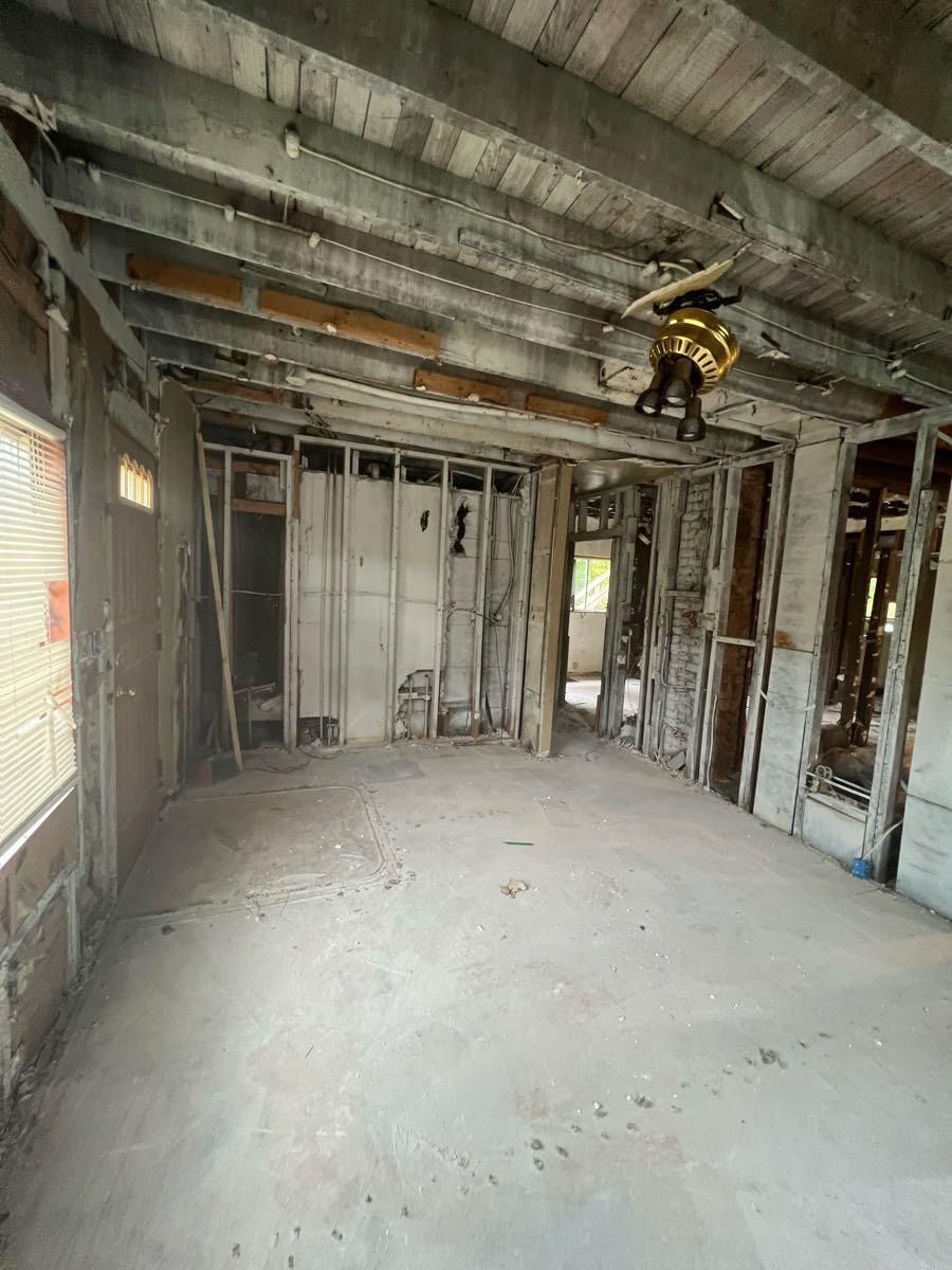 Interior view of a room under construction with exposed beams, studs, and concrete floor.