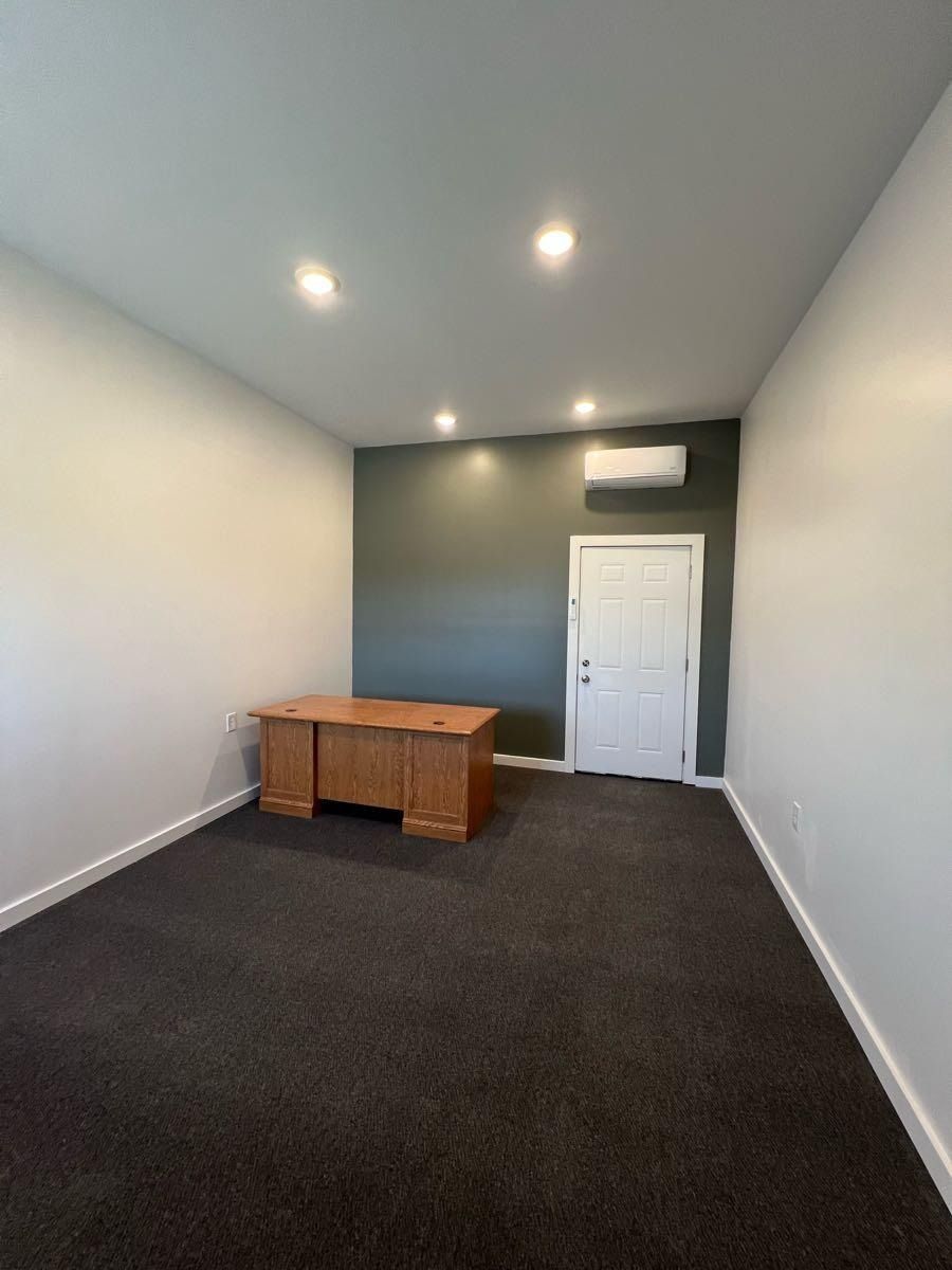 Office room with a wooden desk, door, and dark carpet. The back wall is green.