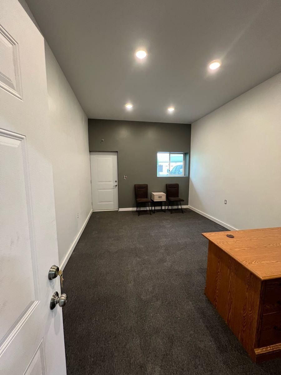 Interior of an empty room with dark carpet, white and gray walls, a window, and two chairs.